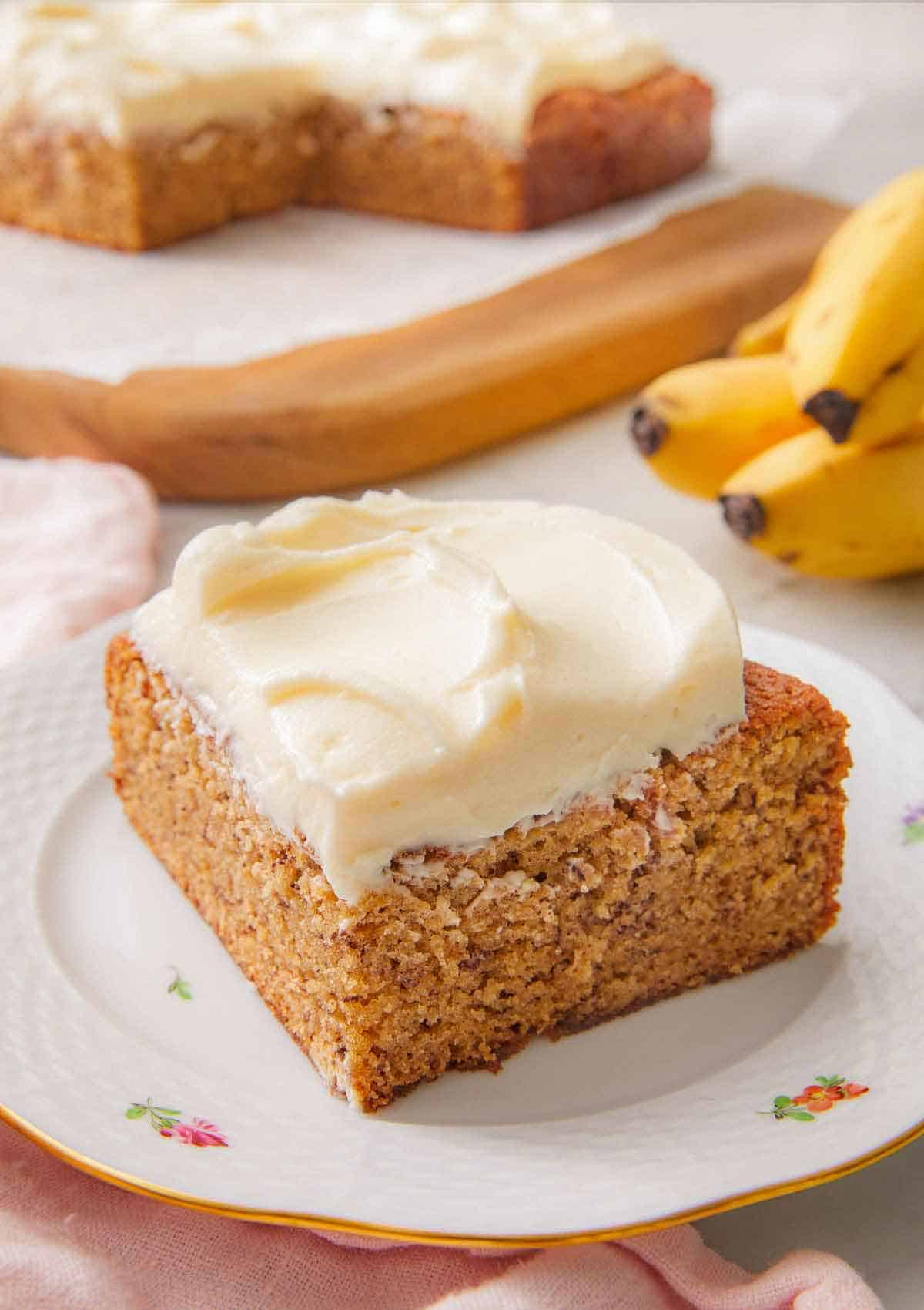 A slice of banana cake with a layer of cream cheese frosting spread on top on a small plate.
