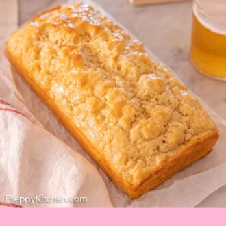 Pinterest graphic of a loaf of beer bread on top of a sheet of parchment with a drink and opened book in the background.