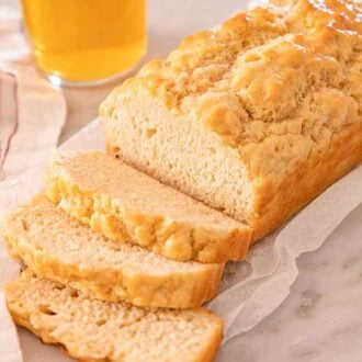 A loaf of beer bread on top of a sheet of parchment with three slices of bread sliced in front.