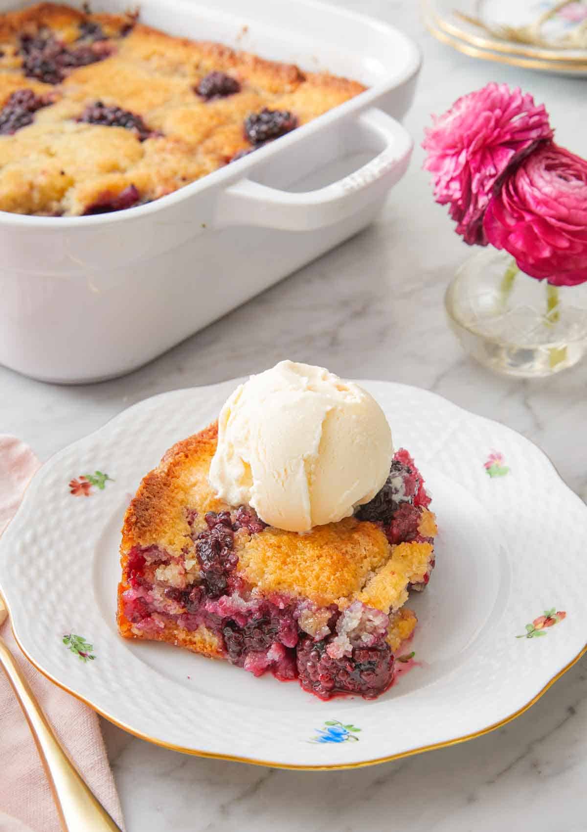 A plate with a serving of blackberry cobbler with a scoop of ice cream on top.