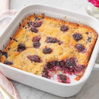 A white baking dish with blackberry cobbler in it, a spoon on the side.