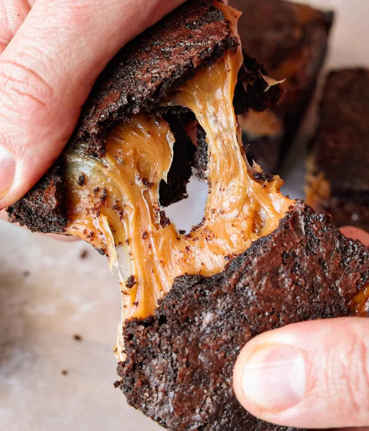A piece of caramel brownie pulled apart, showing the melty caramel center caramel pulling apart.