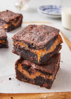Two square pieces of caramel brownies stacked on top of each other on top of a lined cutting board.