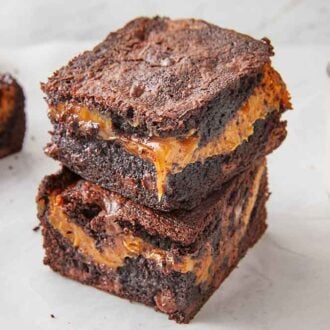 A stack of two caramel brownies with a class of milk and a couple more brownies beside it.