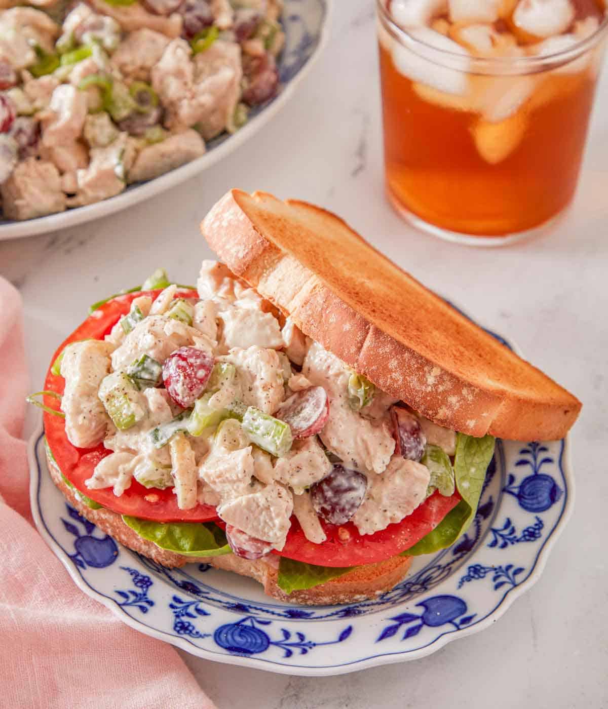 A sandwich filled with chicken salad on a plate with iced tea in the background.