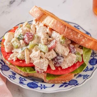 A plate with chicken salad served on bread, lettuce, and sliced tomatoes.