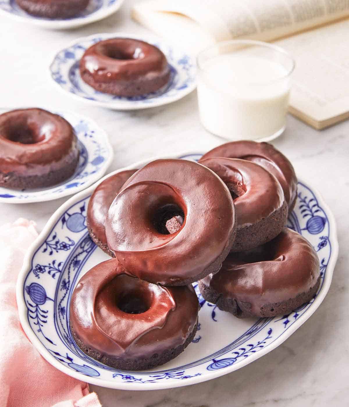 A platter of chocolate donuts with a glass of milk and additional plated donuts in the back.