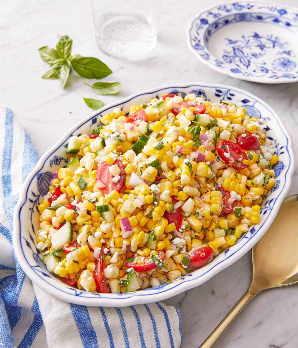 A platter of corn salad with a large golden serving spoon beside it.