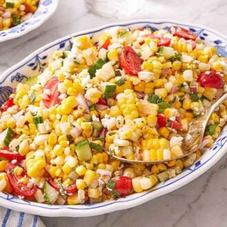 A large platter of corn salad with a serving spoon tucked in.