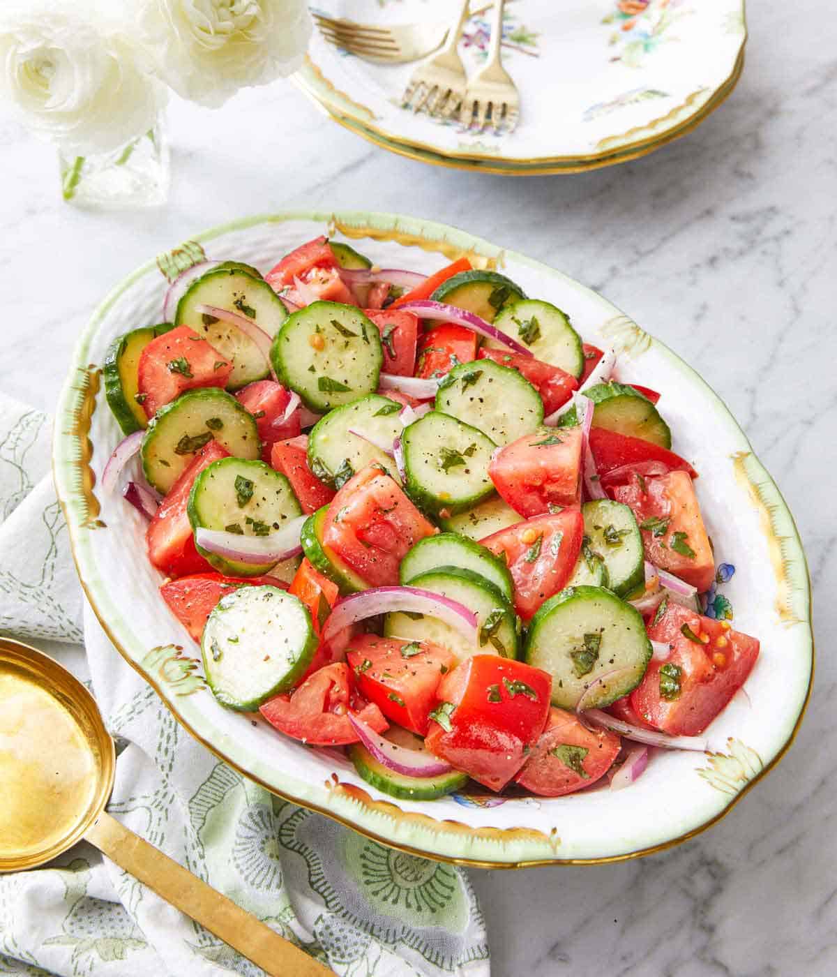 An oval platter of cucumber tomato salad with a serving spoon beside it.