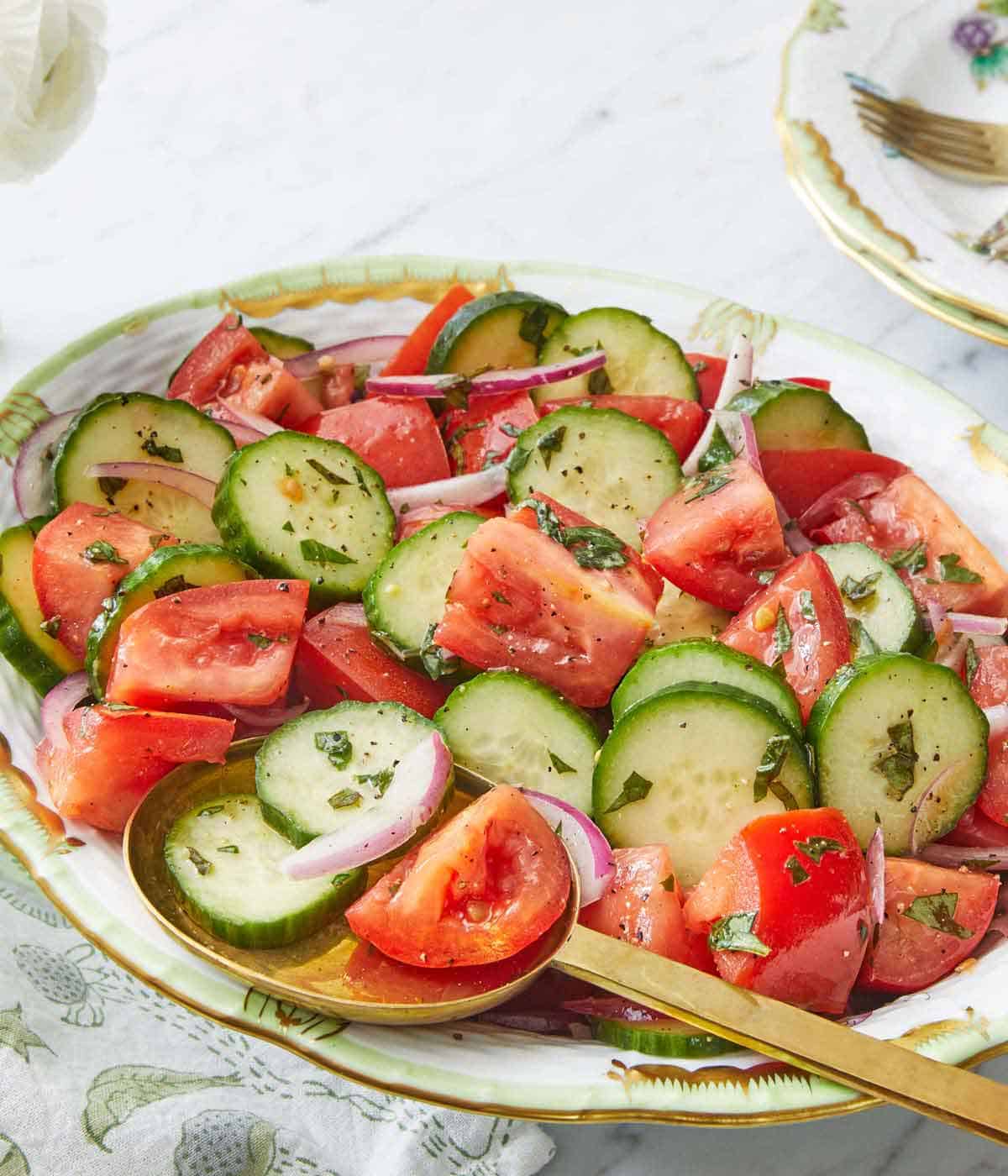 A platter of cucumber tomato salad with a serving spoon tucked underneath.