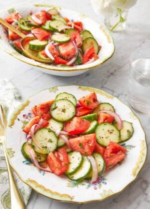 A plate of cucumber tomato salad with a platter full in the background.