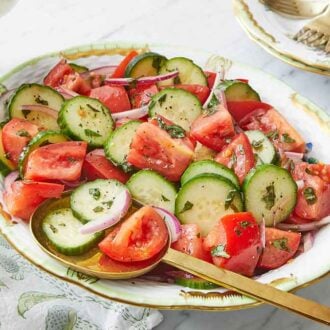 An oval platter of cucumber tomato salad with a golden serving spoon inside.