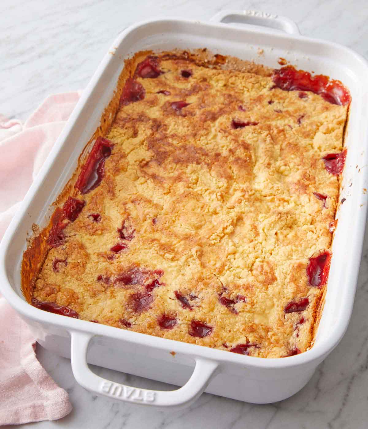 A dump cake inside of a white baking dish with a pink linen napkin on the side.