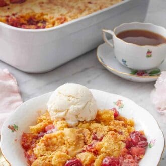 Pinterest graphic of a bowl with a serving of dump cake with a scoop of ice cream on top with a baking dish and cup of tea in the back.