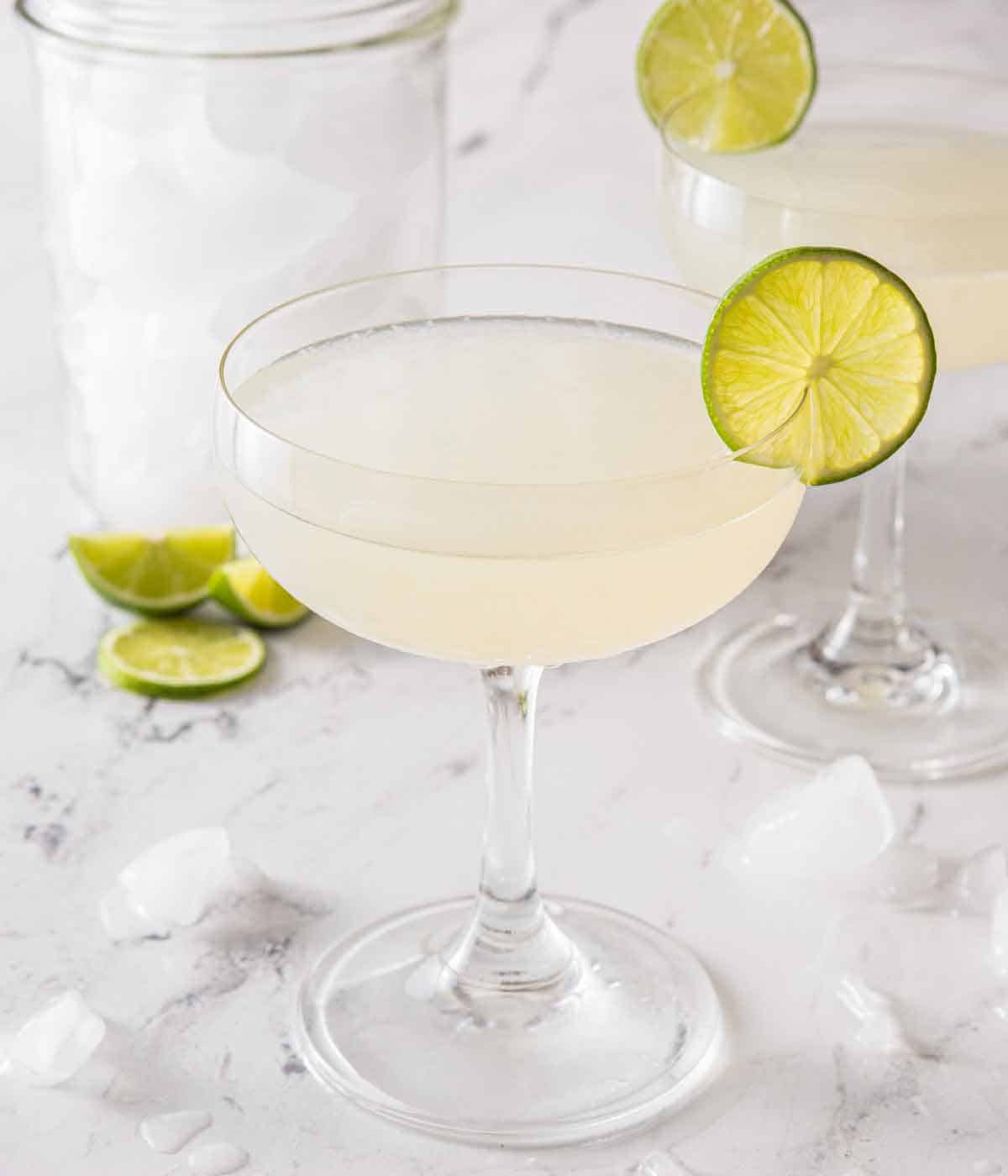 Two gimlet with one pulled front and center with a container of ice and more limes in the back.