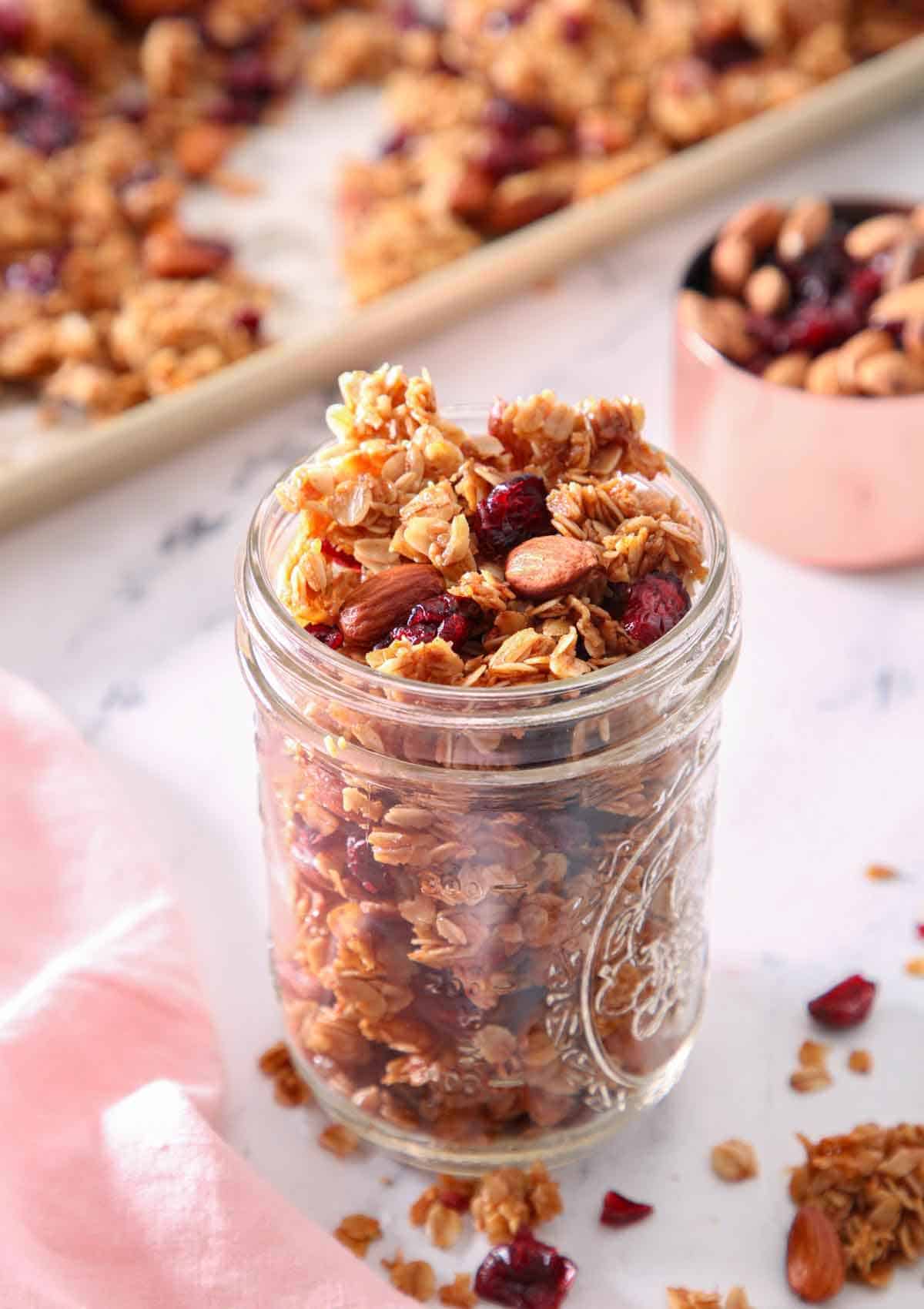 A mason jar filled with granola with a sheet pan with granola in the background, out of focus.