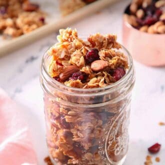 Pinterest graphic of a mason jar of granola with more scattered around with a measuring cup and sheet pan with granola in the back.