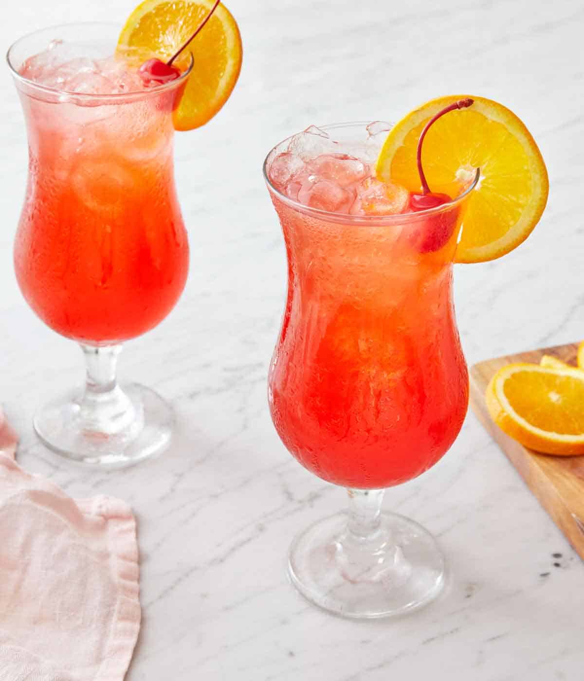 Two glasses of hurricane drink with an orange slice and cherry as a garnish.
