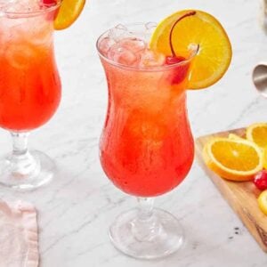 Two glasses of the cocktail hurricane drink with garnish in the drink and on a wooden cutting board.