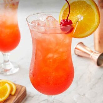 Pinterest graphic of a glass of hurricane cocktail with a cherry and orange slice garnish with a jigger and shaker in the background.