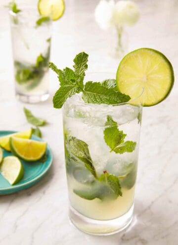 A glass of mojito with a lime and mint garnish on the rim of the glass.