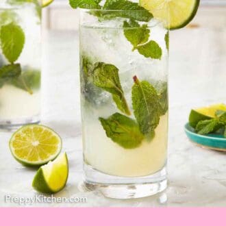 Pinterest graphic of a glass of mojito with lime and mint on the edge of the glass. Freshly cut limes on the counter beside it.
