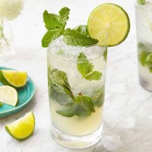 Two glasses of mojitos with one in the middle in focus. A small plate of garnish on the side.