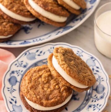 A plate with two oatmeal cream pies with a platter with more along with a glass of milk in the background.