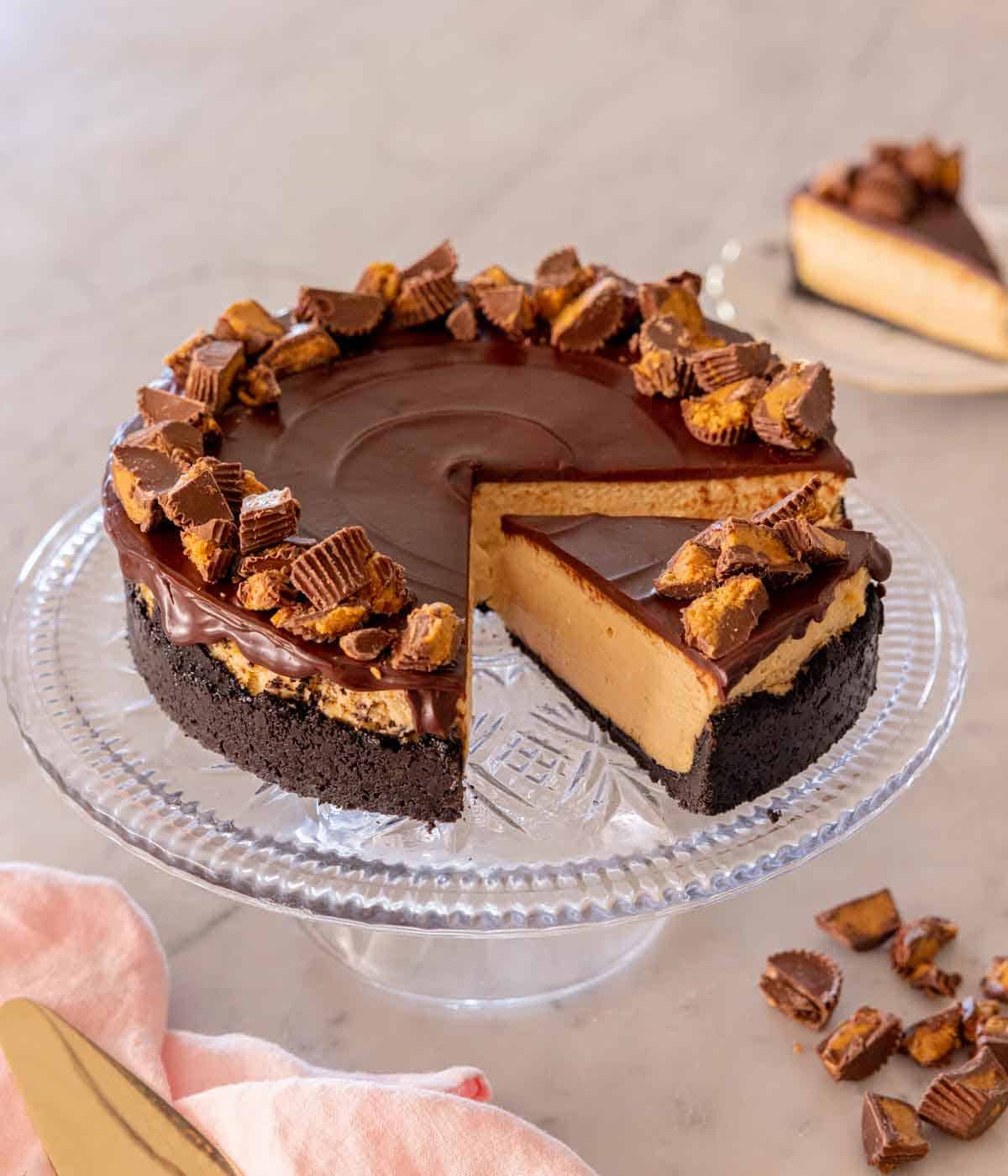 A cake stand with a peanut butter cheesecake with one slice removed and a second slice cut.