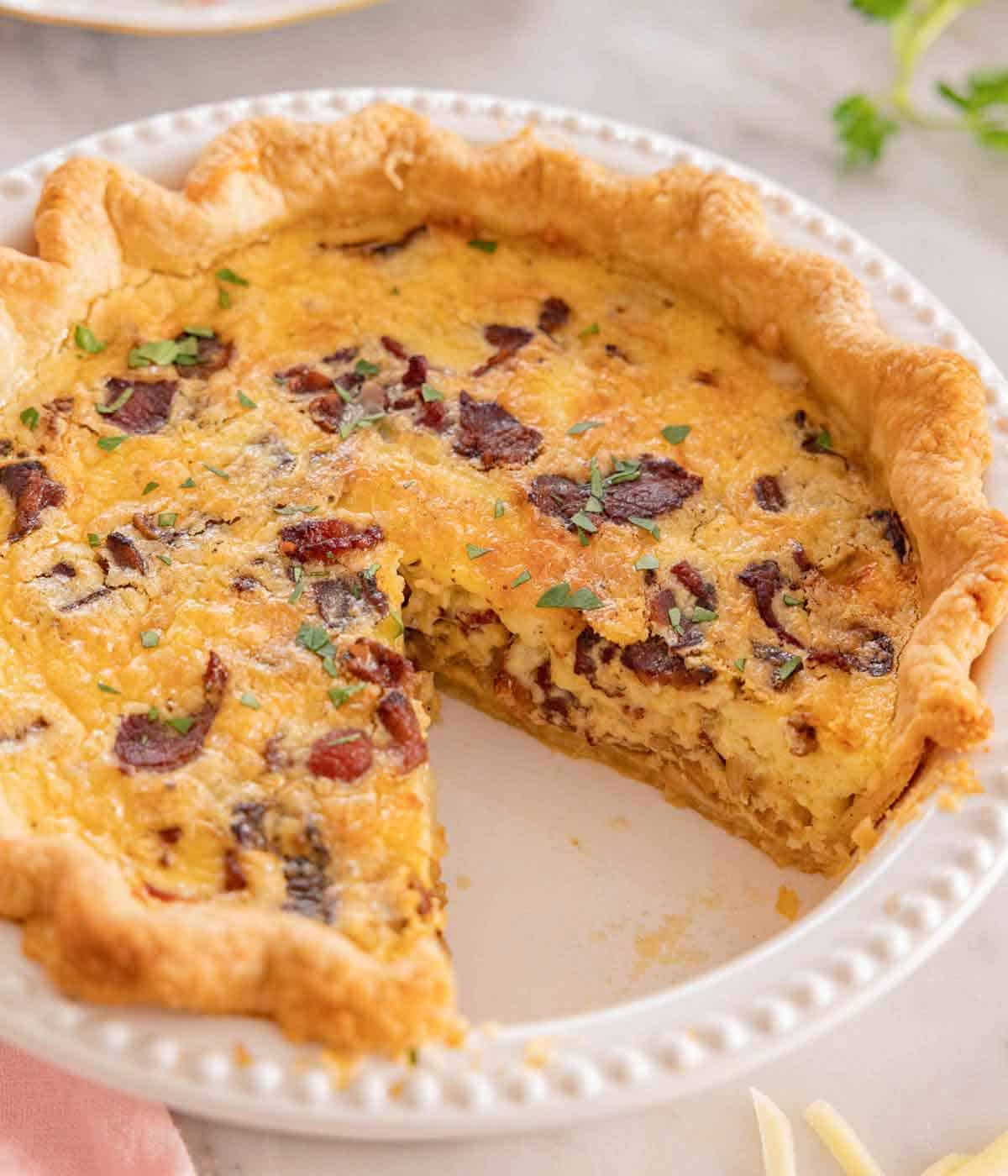 A quiche Lorraine in a pie dish with a slice removed.