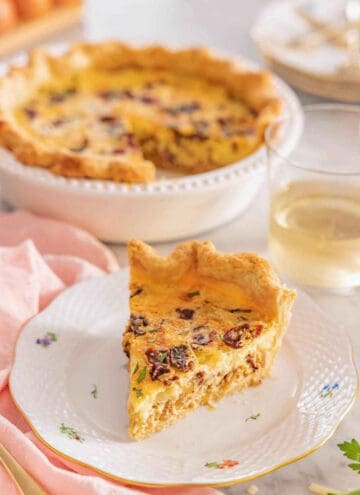 A plate with a slice of quiche Lorraine with the rest of the quiche in the background.