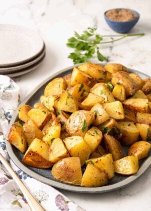 A platter of roasted potatoes with fresh parsley as garnish and in the background with ground pepper.