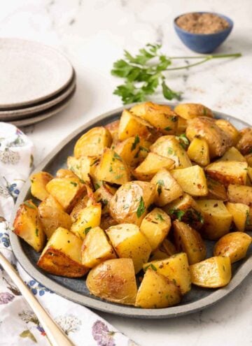 A platter of roasted potatoes with fresh parsley as garnish and in the background with ground pepper.