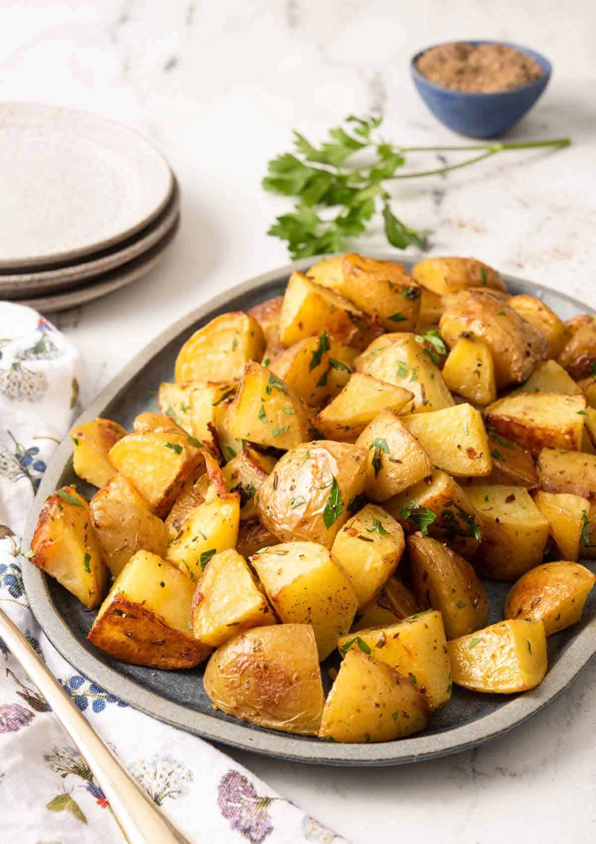 A platter of roasted potatoes with fresh parsley as garnish and in the background with ground pepper.