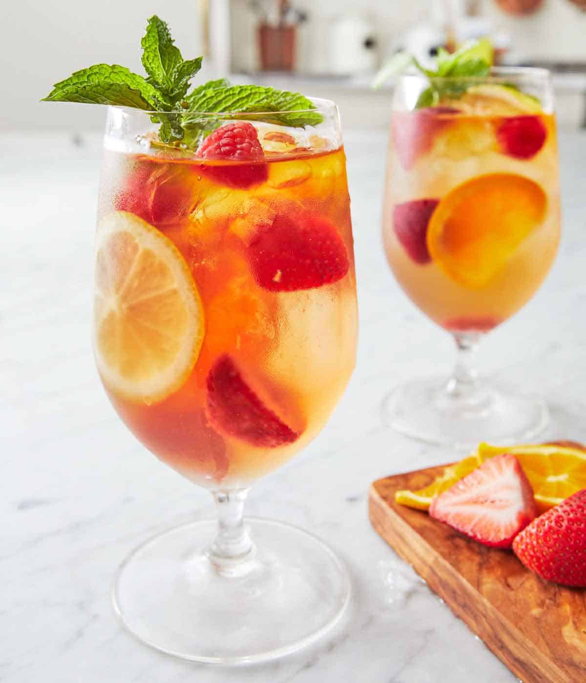 Two glasses of rose sangria with fresh mint on top. A small cutting board with sliced strawberries and oranges on the side.