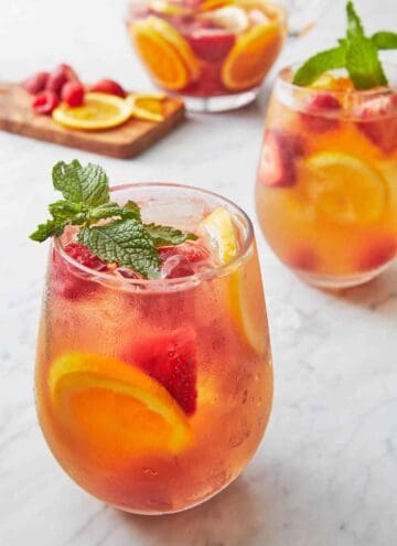 Two glasses of rose sangria with fresh mint as garnish and cut fruit in the background.