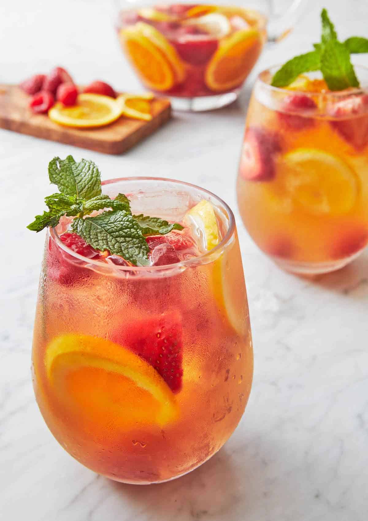 Two glasses of rose sangria with fresh mint as garnish and cut fruit in the background.