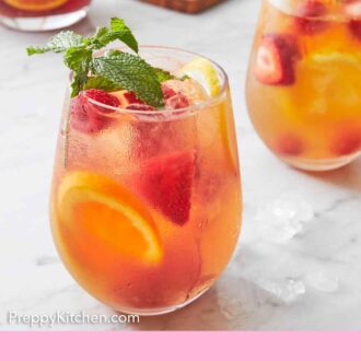 Pinterest graphic of two glasses of rose sangria with cut fruit and a pitcher in the background.