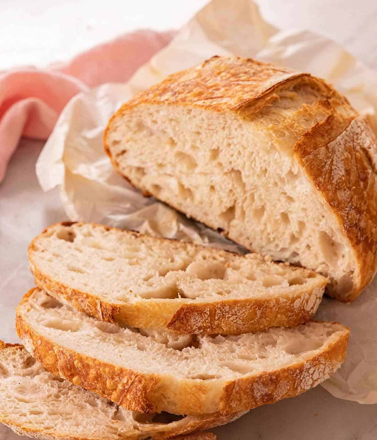 A loaf of sourdough bread with three slices cut in front of the loaf.