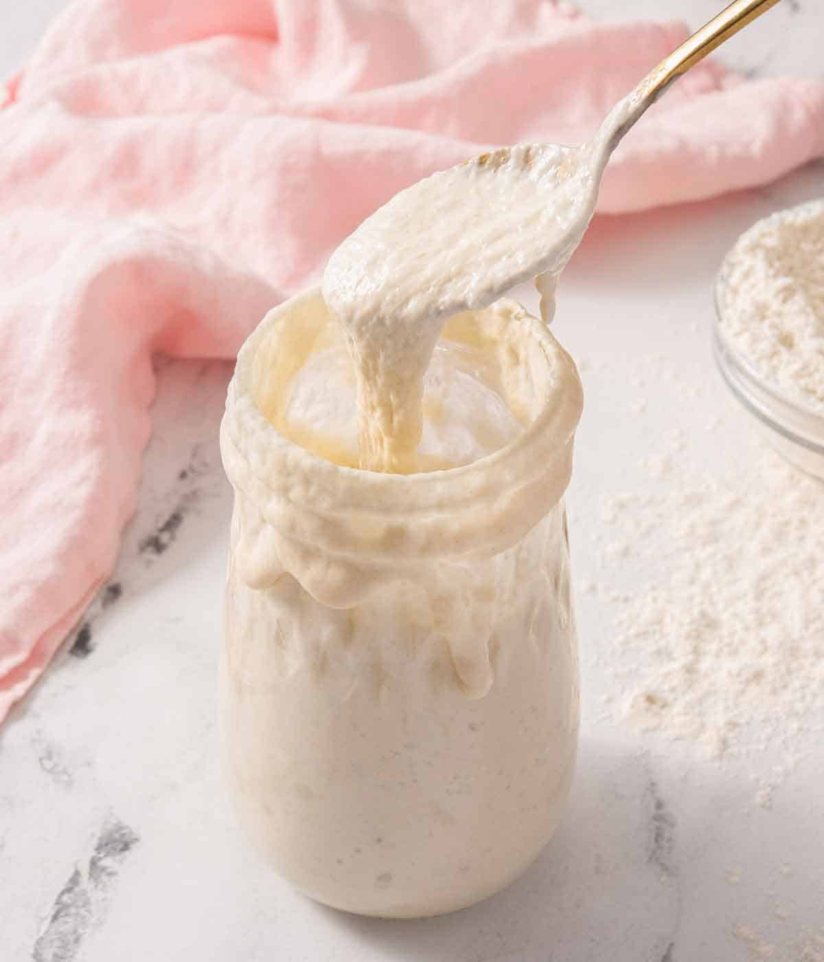 A mason jar of sourdough starter with a spoon scooping some out.