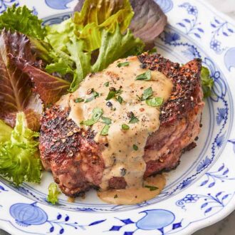 A plate with steak au poivre with fresh chopped parsley garnished on top with a side of greens.