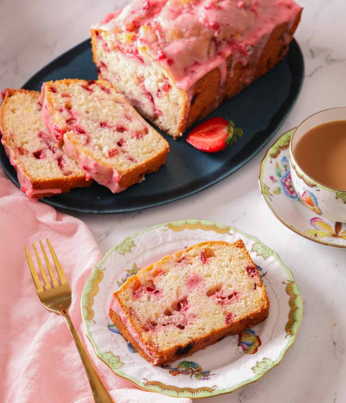 A slice of strawberry bread on a plate with a platter with cut slices in the back.