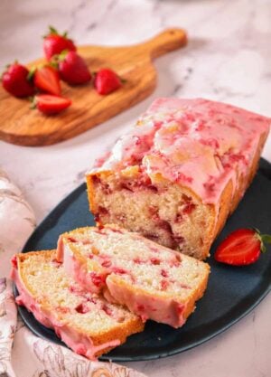 A loaf of strawberry bread on a blue platter with two slices cut in front.