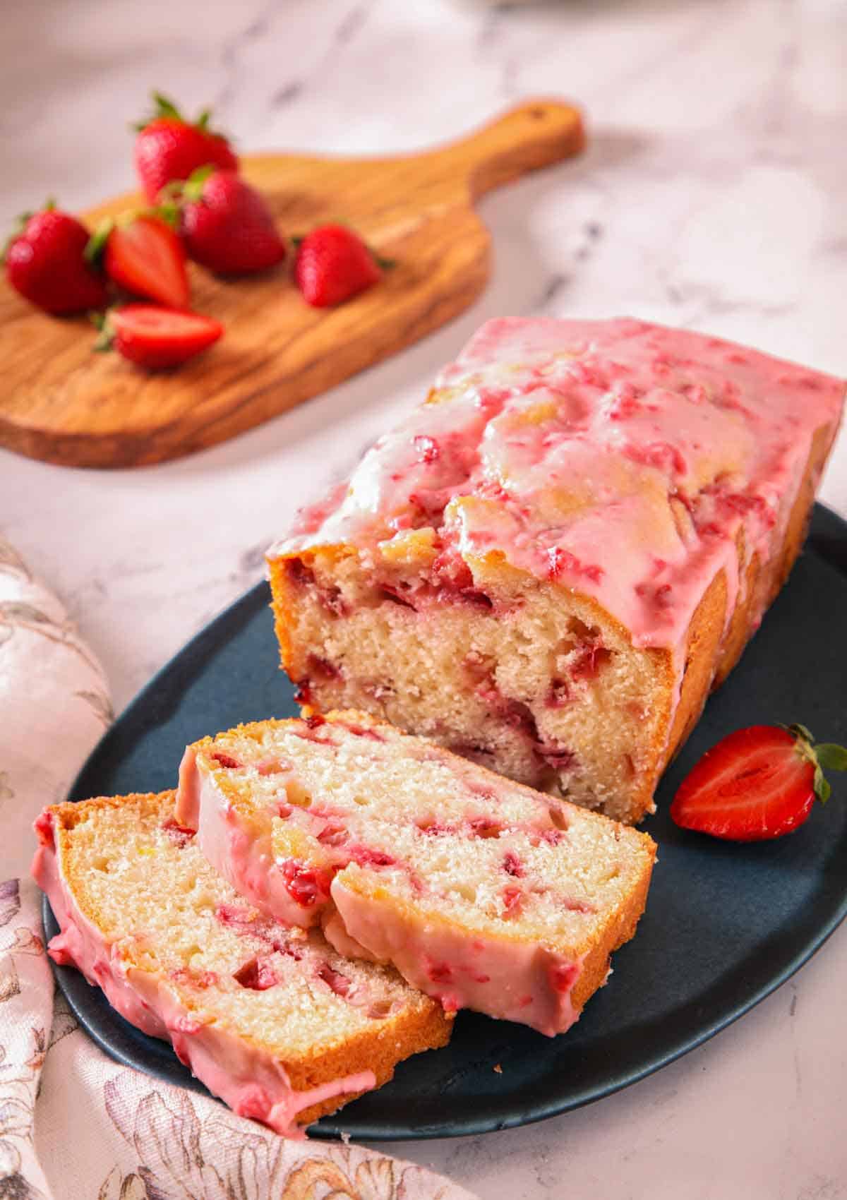 A loaf of strawberry bread on a blue platter with two slices cut in front.