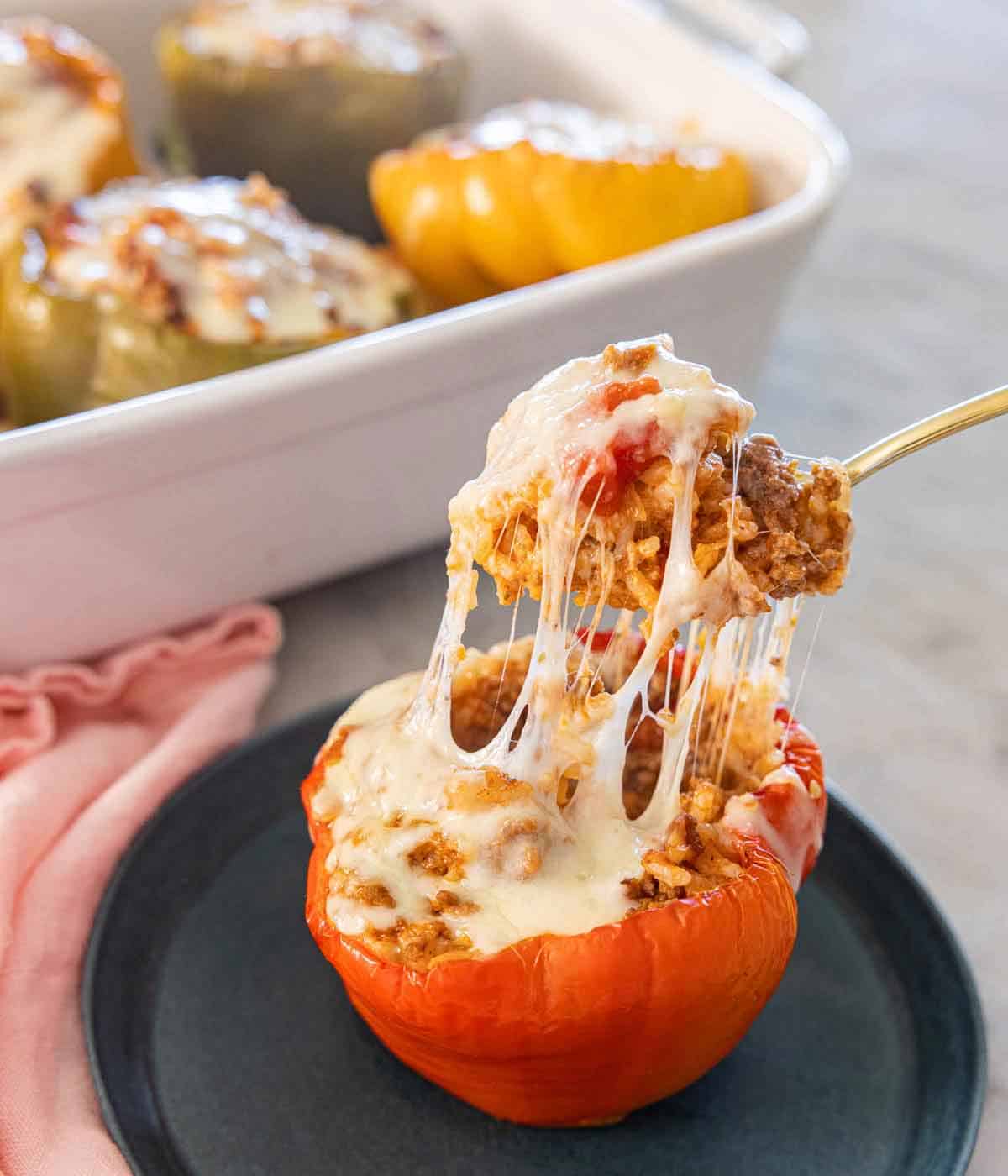A plate with a forkful of filling lifted up from a stuffed pepper with the melted cheese pulling away from the pepper.
