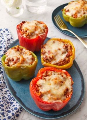 A platter with four stuffed peppers with a plate with a single one in the background.