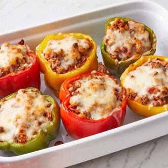 A white baking dish with six stuffed peppers with melted cheese on top.