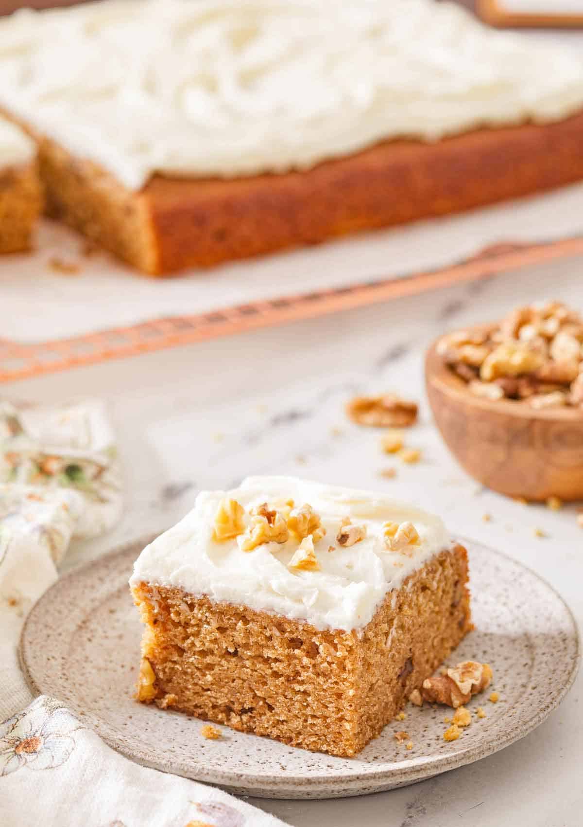 A plate with a piece of applesauce cake with some chopped walnuts on the frosting.