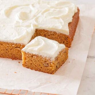 An applesauce cake with frosting on a lined cooling rack with one square piece cut.